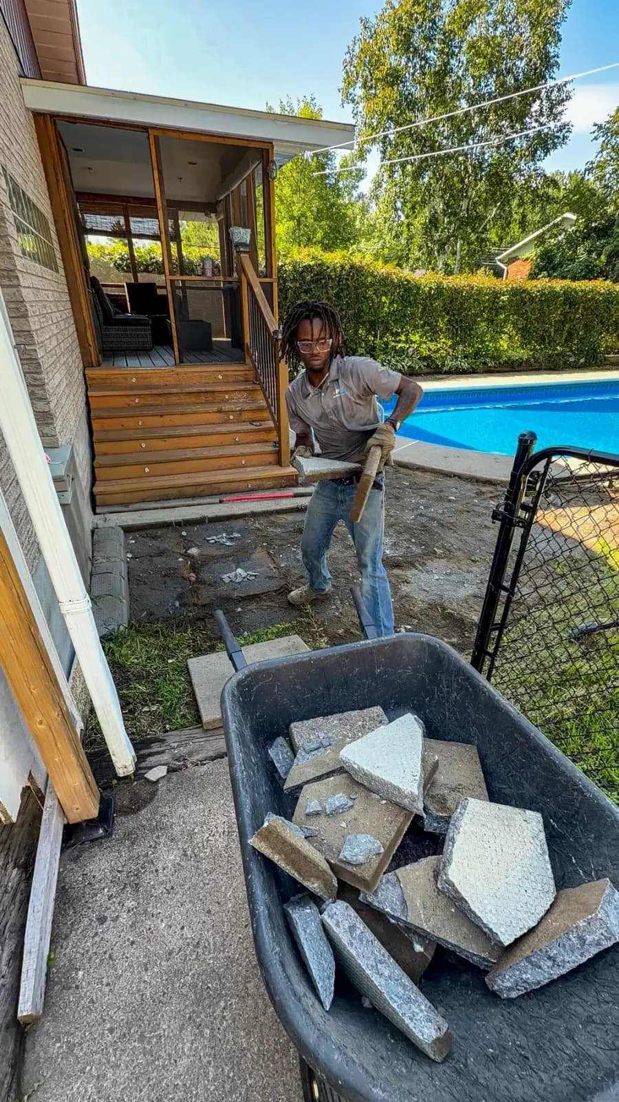 PVS crew member loading broken patio slabs into a wheelbarrow beside the pool