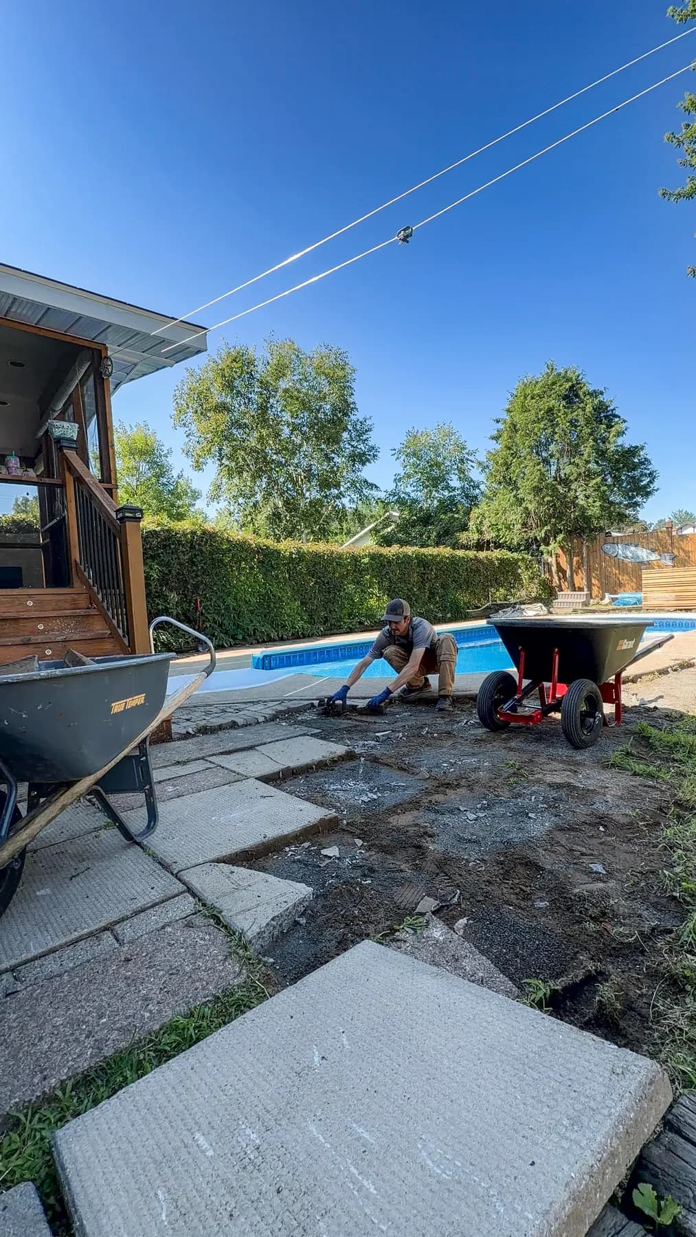 Crew member prying up old patio slabs beside the pool during demolition