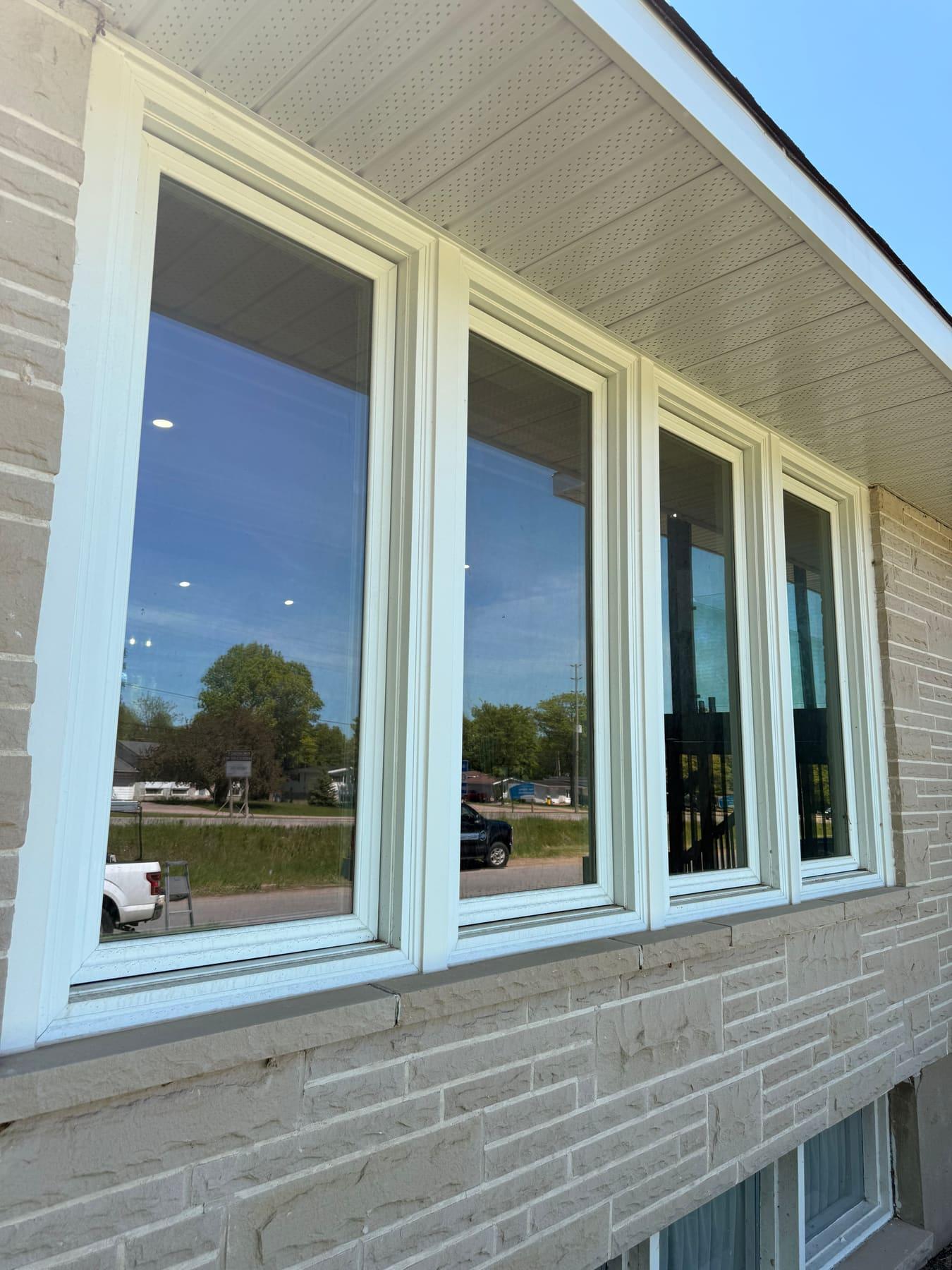 A row of four large picture windows reflecting blue sky, trees, and a PVS truck after exterior cleaning