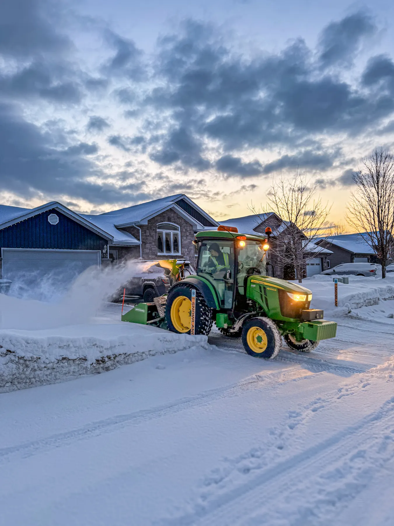 PVS tractor snow-blowing a residential driveway at sunrise after an overnight storm